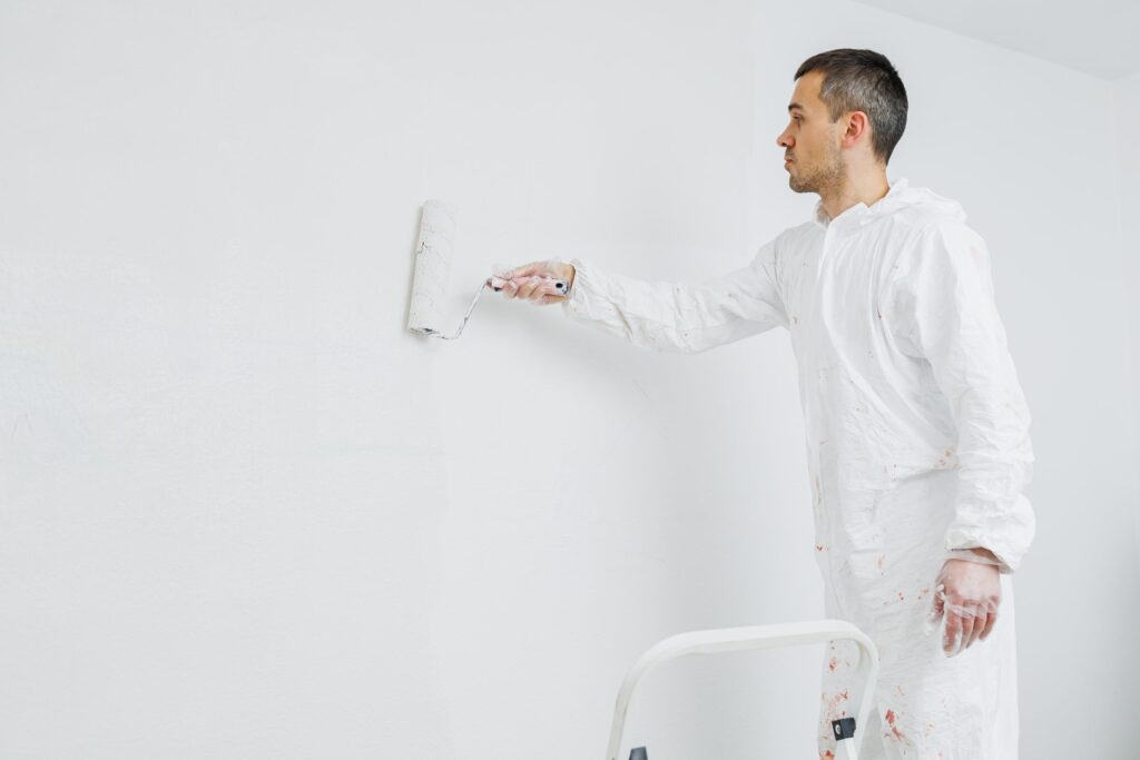 Painter applying a smooth coat of white paint on a wall with professional equipment.